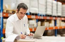 Photo d'un homme en chemise blanche prenant des notes dans un entrepôt logistique