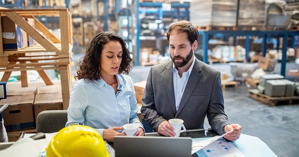 Photo de deux managers analysant des documents devant un ordinateur en entrepôt