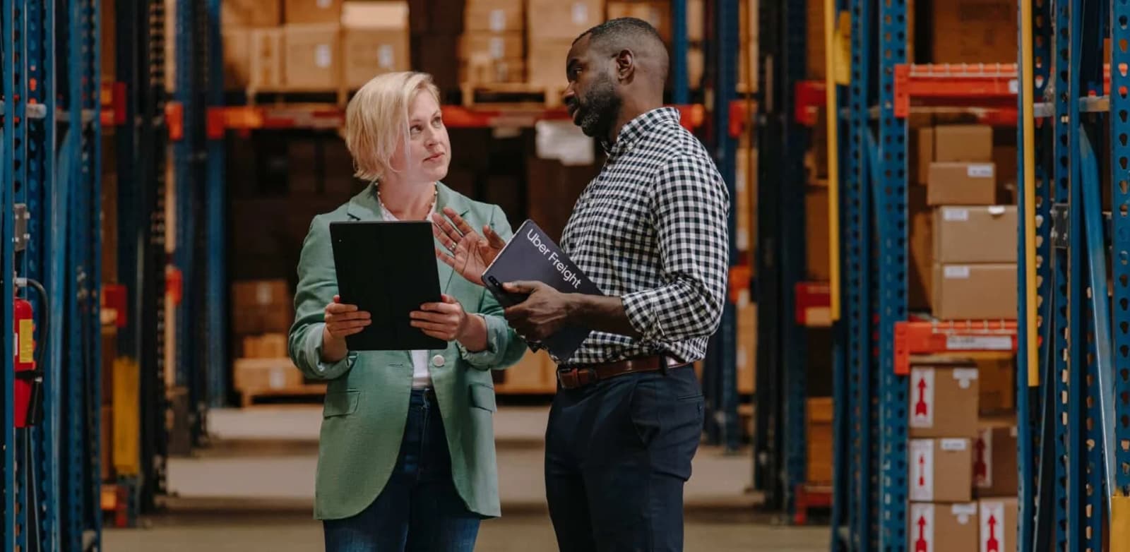 Photo de deux professionnels echangeant avec tablettes dans une allee d'entrepôt logistique