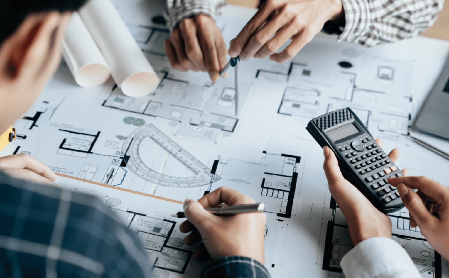 Photo de mains de professionnels analysant des plans d'architecte avec calculatrice et rapporteur