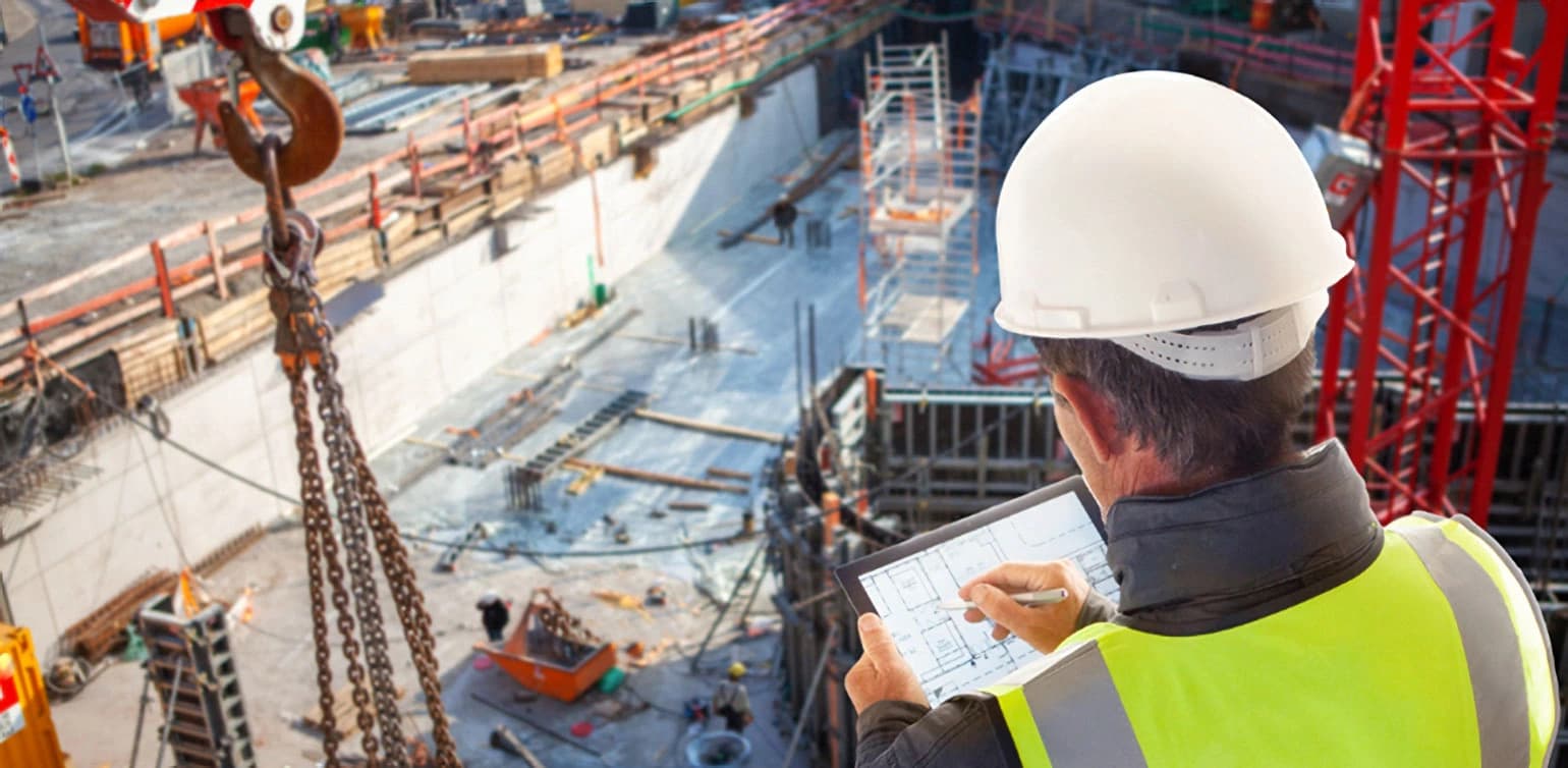 Photo d'un ingénieur en casque et gilet jaune consultant des plans sur tablette sur un chantier