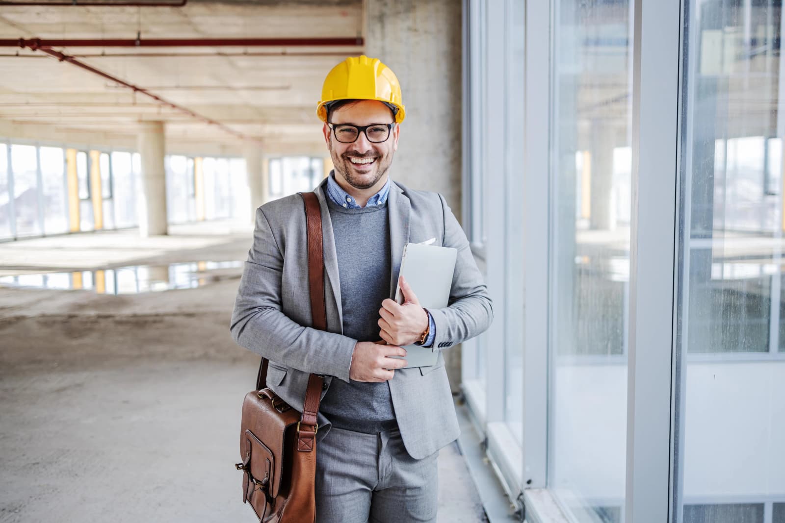 Photo d'un ingénieur souriant avec casque jaune et sacoche dans un bâtiment en construction