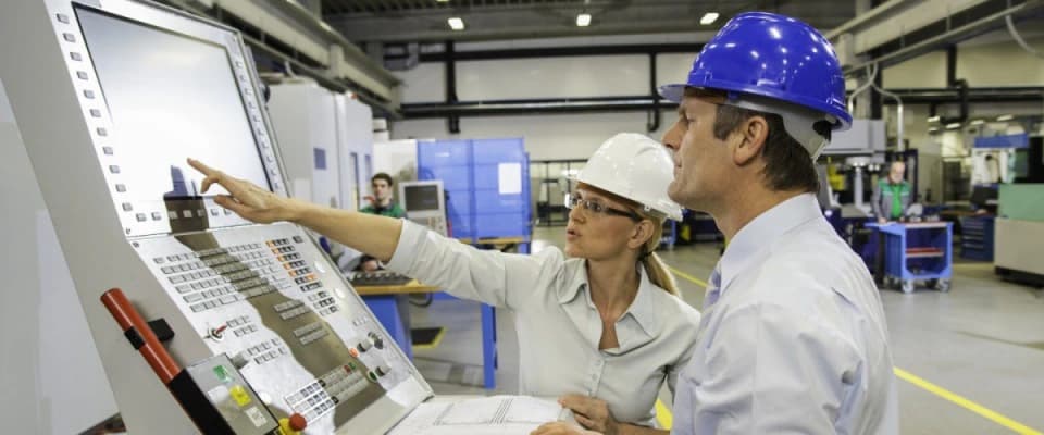 Photo de deux ingénieurs casqués analysant un panneau de commande dans une usine industrielle