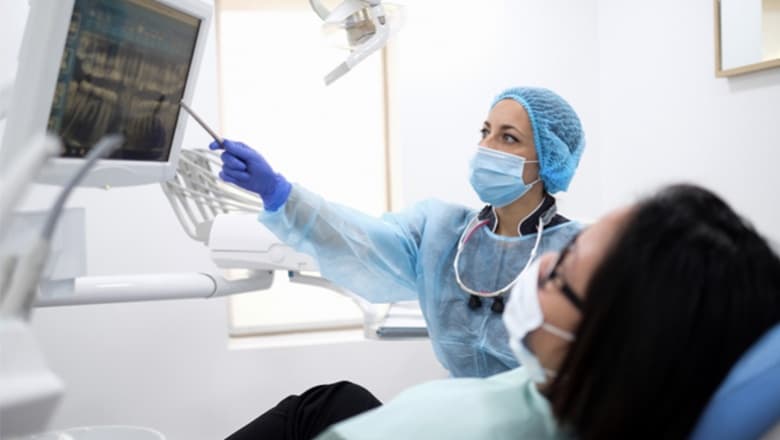 Photo d’une dentiste montrant une radiographie dentaire sur écran à une patiente allongée