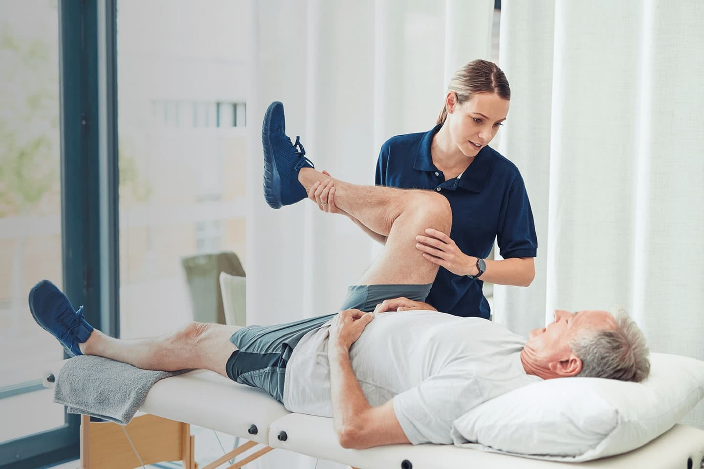 Photo d'une kinésithérapeute en polo bleu marine manipulant le genou d'un patient allongé sur une table