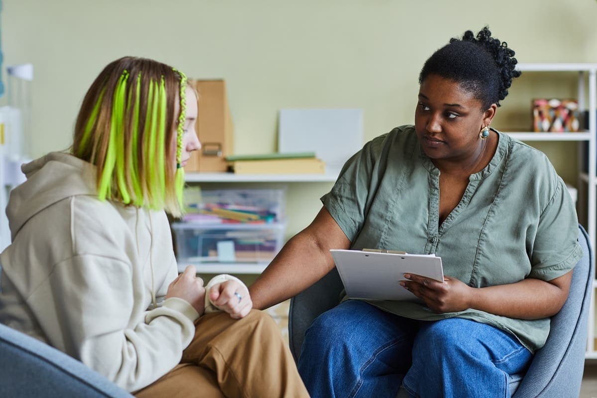 Photo d'une psychologue avec un bloc-notes en consultation avec une jeune patiente assise en fauteuil