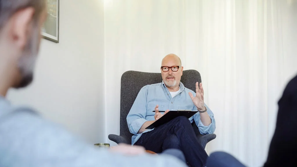 Psychiatre en consultation avec un patient, assis dans un fauteuil avec un bloc-notes dans son cabinet