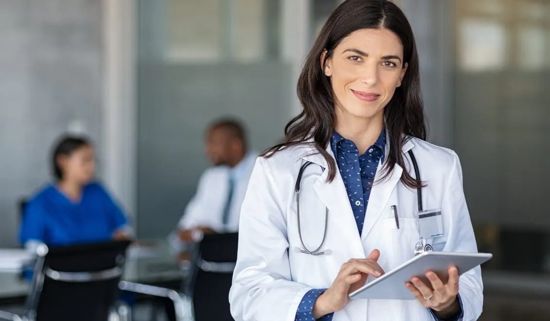 Photo d'une femme médecin brune en blouse blanche tenant une tablette dans un environnement hospitalier