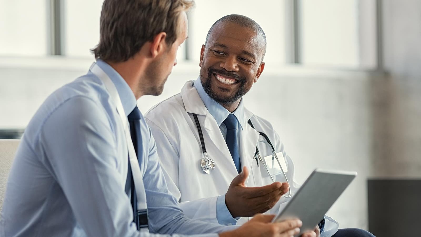 Photo d'un médecin en blouse blanche avec stéthoscope échangeant sur une tablette avec un collègue