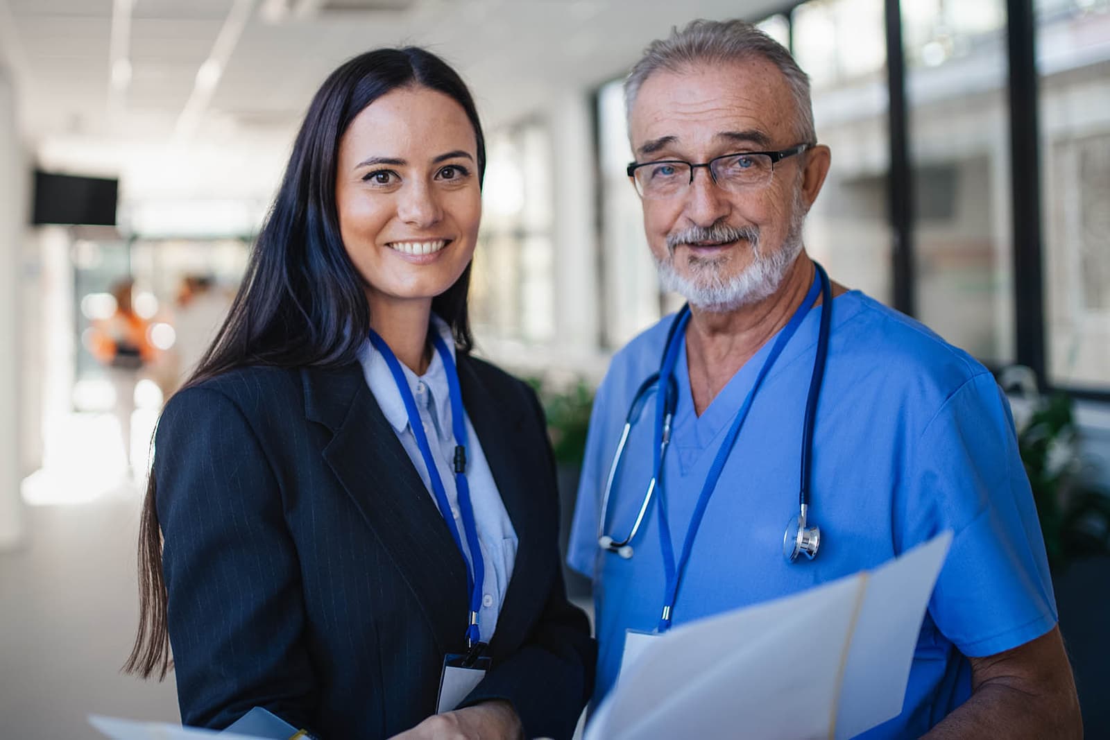 Photo d’une professionnelle en tailleur et d’un médecin senior en blouse bleue dans un couloir hospitalier