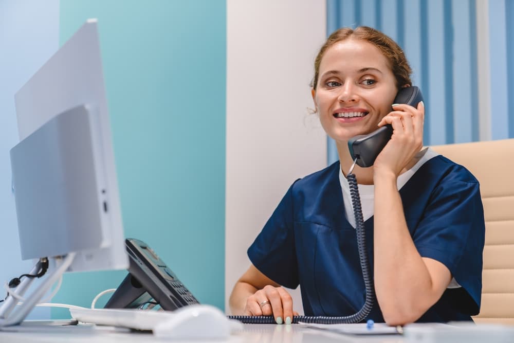Photo d’une secrétaire médicale souriante répondant au téléphone devant son ordinateur de bureau