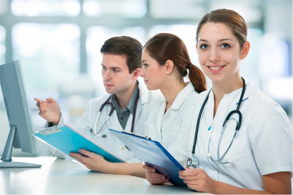 Photo de trois professionnels de santé en blouse blanche avec dossiers devant un écran d’ordinateur