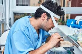 Photo d’un prothésiste dentaire travaillant avec précision sur une prothèse dans son laboratoire