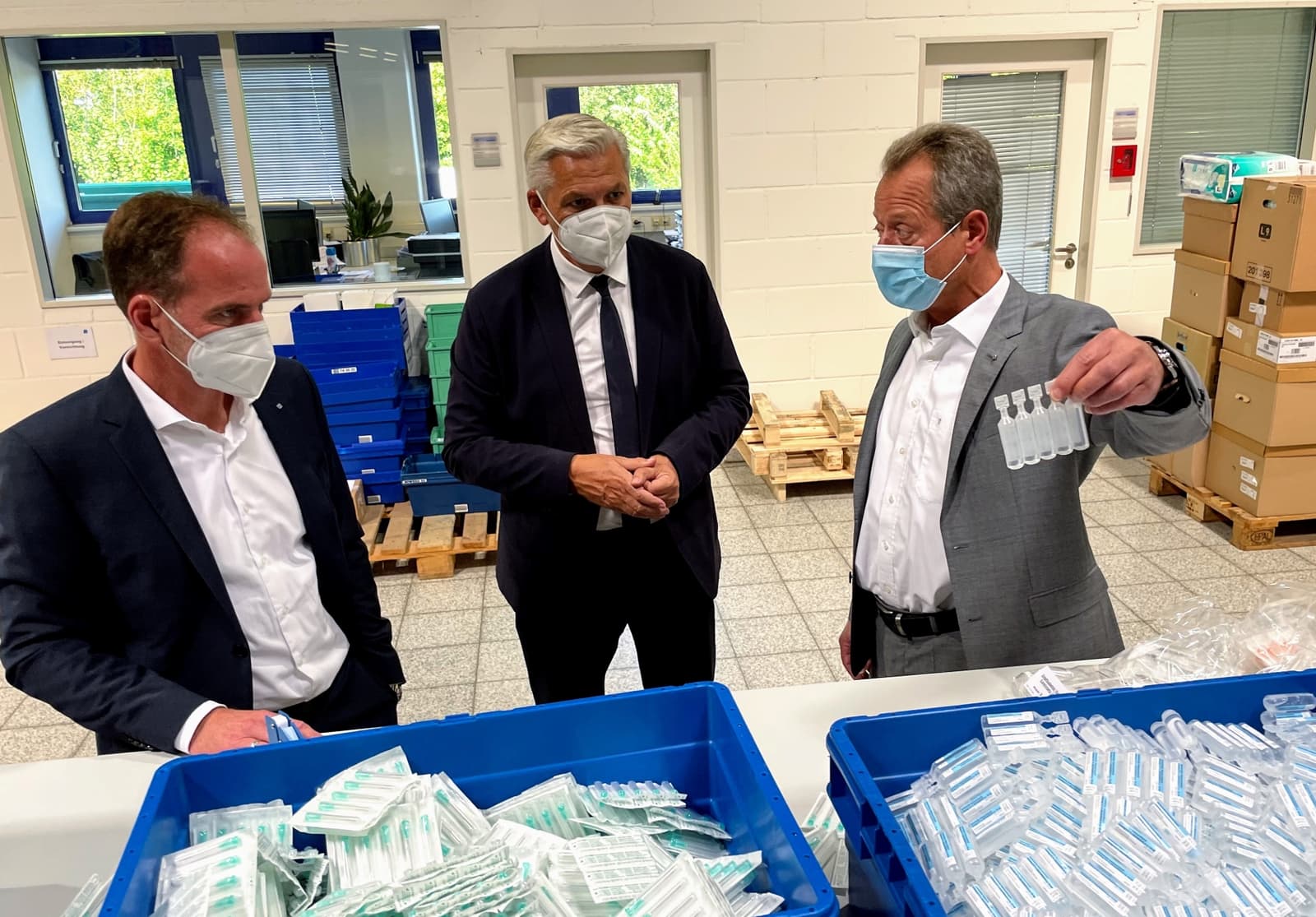 Photo de trois hommes masqués inspectant des produits pharmaceutiques dans un entrepôt de production
