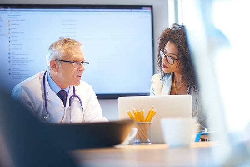 Photo d’un médecin senior et d’une collaboratrice travaillant ensemble devant un ordinateur portable