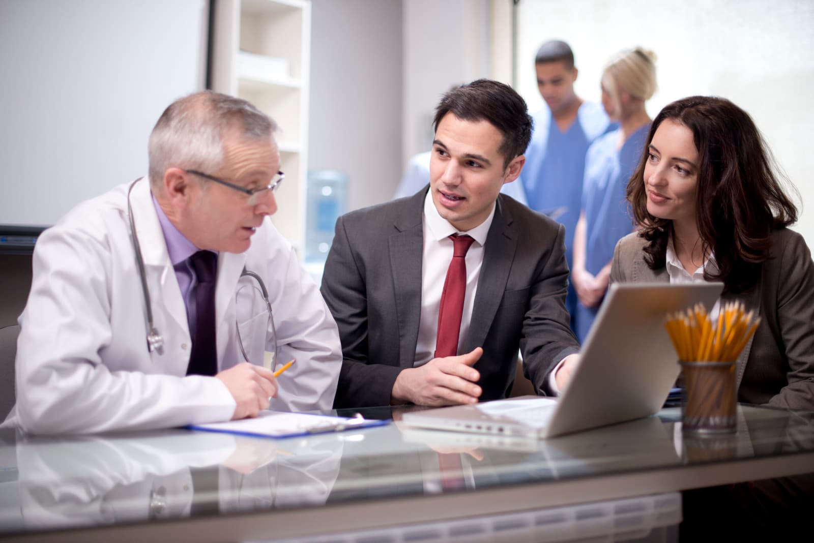Photo d’un médecin et de deux professionnels en costume discutant devant un ordinateur portable